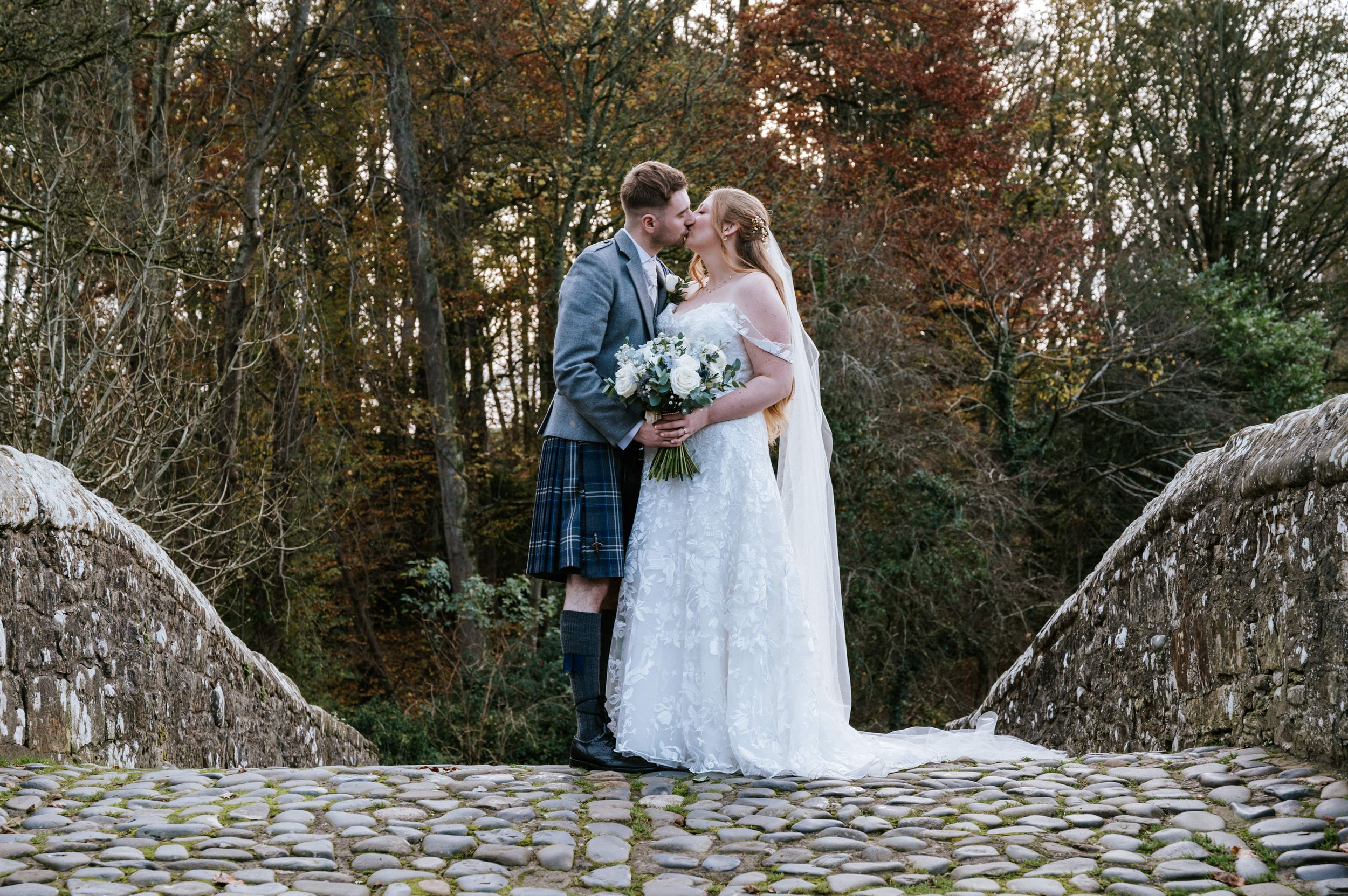 A wedding couple stands on a historic cobblestone street beside traditional stone buildings.