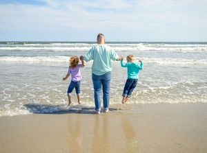 Family walking along the shoreline together as waves crash on a sunny beach day.