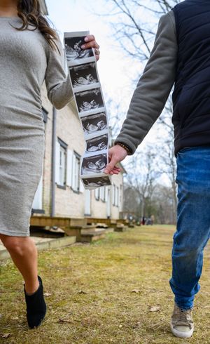 Couple holding ultrasound photos while walking on grass outside a house in winter.