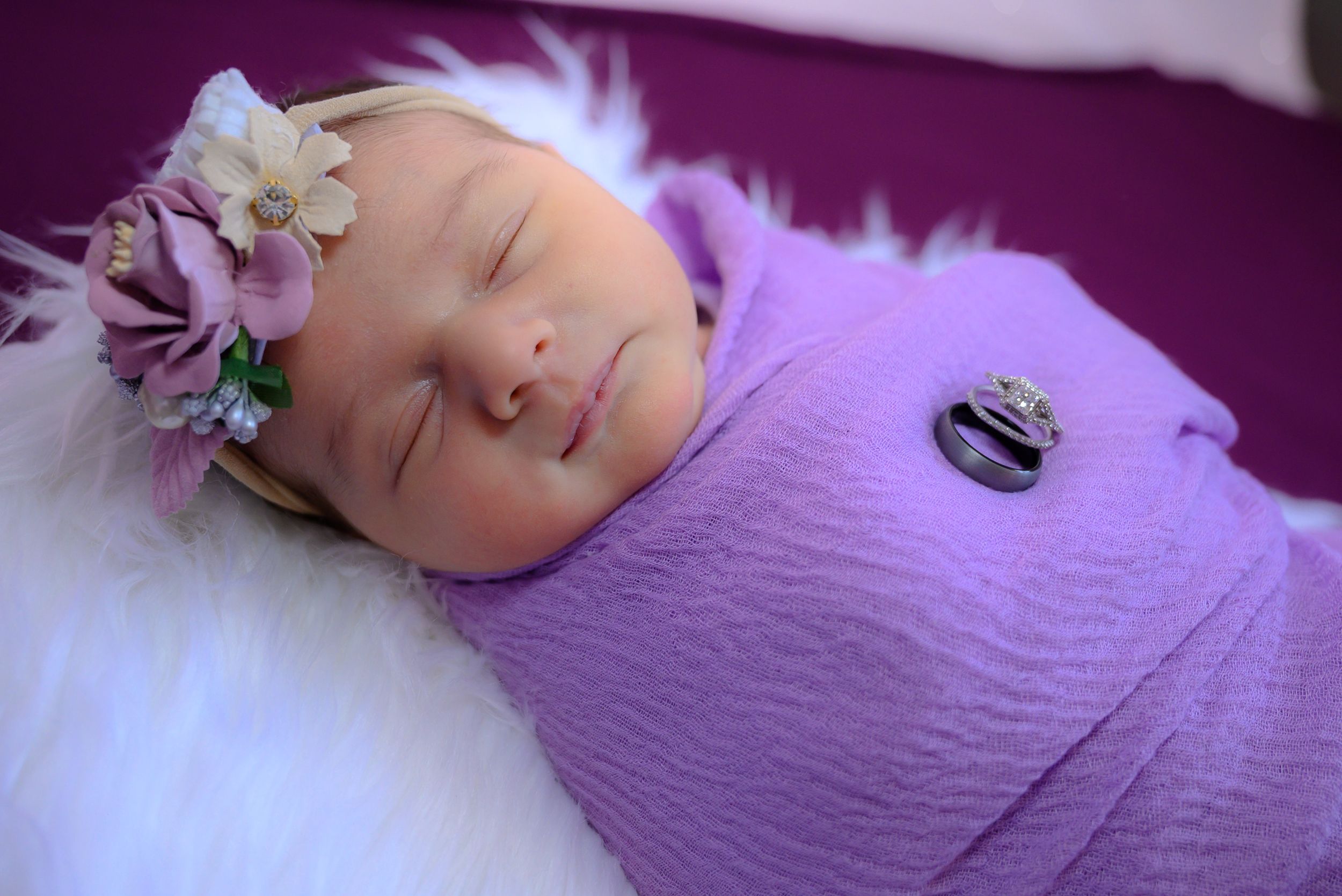A newborn baby wearing a purple onesie rests peacefully on a soft surface.