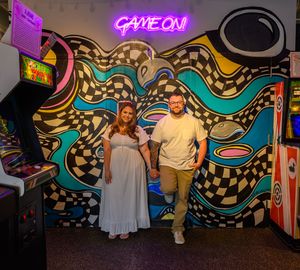 People posing in front of a vibrant graffiti wall with neon lights and colorful geometric patterns in an arcade setting.
