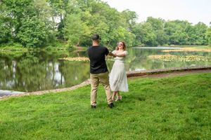 A couple walks hand in hand along a lush green riverbank on a peaceful summer afternoon.
