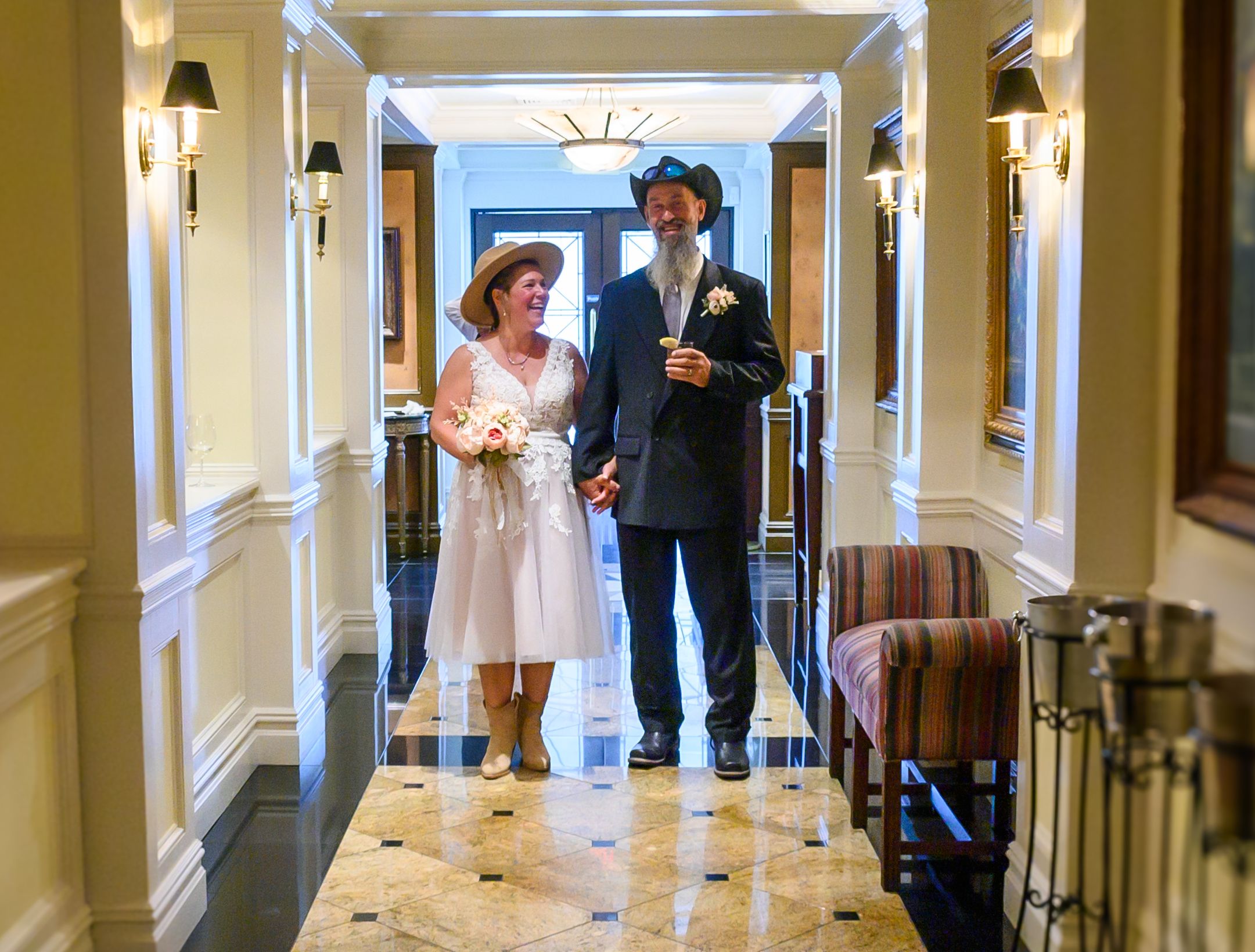 A couple walks down an elegant hallway with white columns and marble floors.