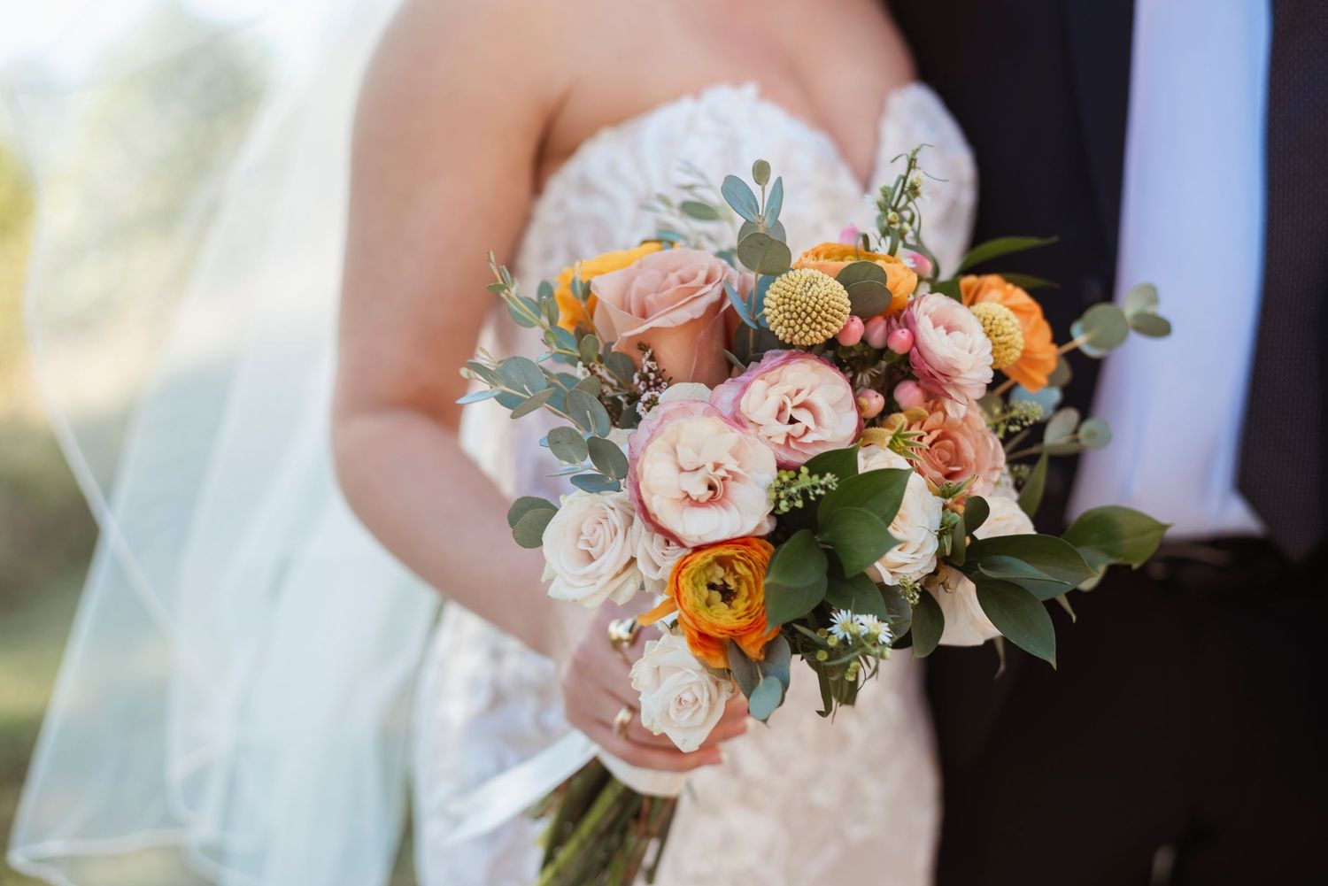 A close-up of a bridal bouquet featuring pink and peach roses with greenery.