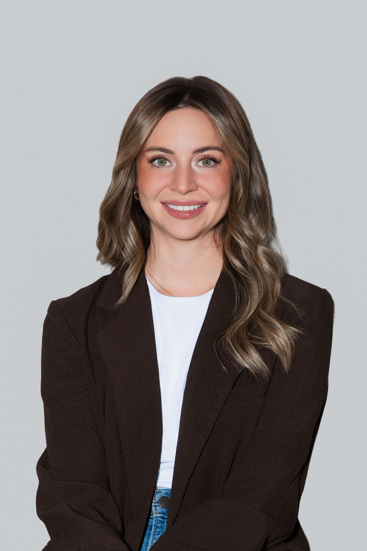 Smiling young woman with highlighted hair wearing a black sleeveless turtleneck top against a gray background.
