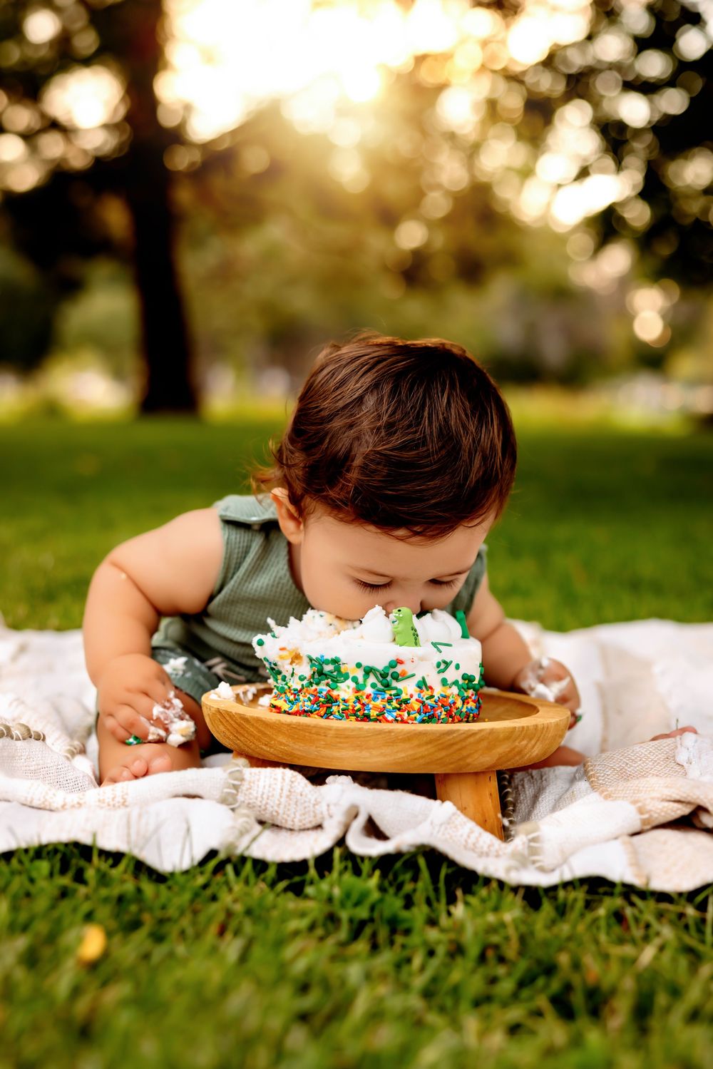 Baby lying on grass near birthday cake smashes face into frosting during golden hour photo session.