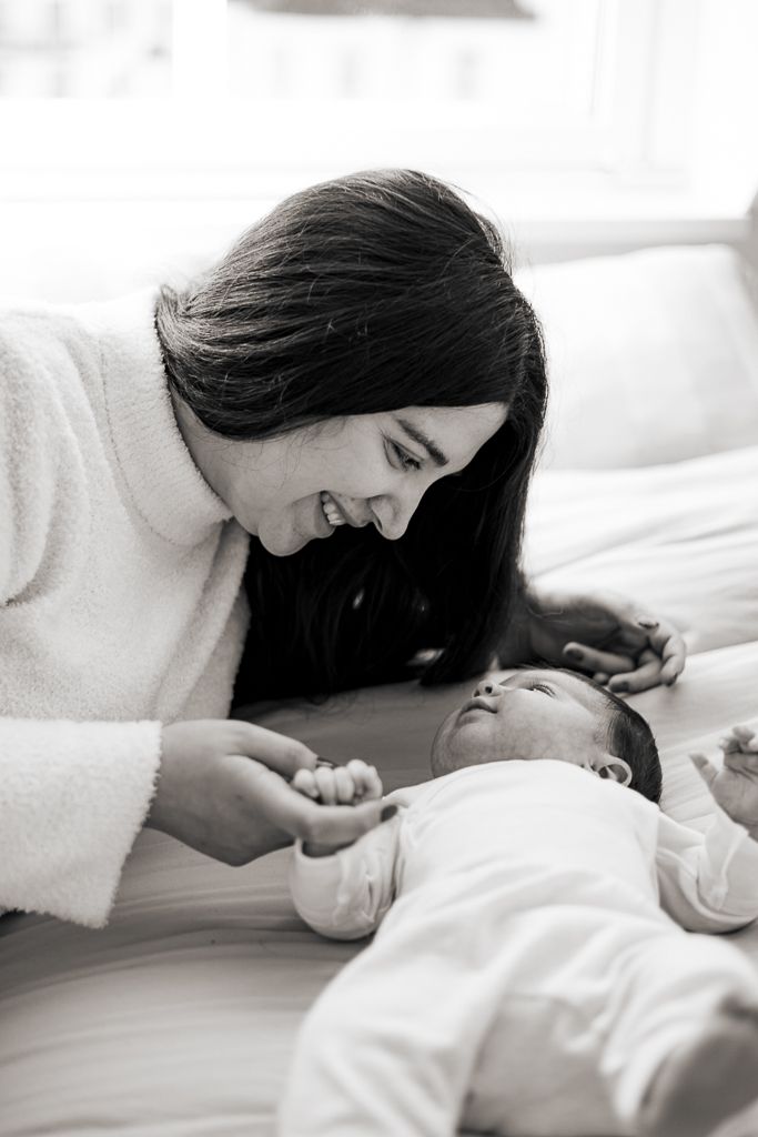 A parent practices skin-to-skin contact with their newborn baby while relaxing on a couch under warm string lights and stars.