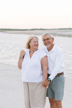 Husband and wife standing close and smiling at one another on the beach
