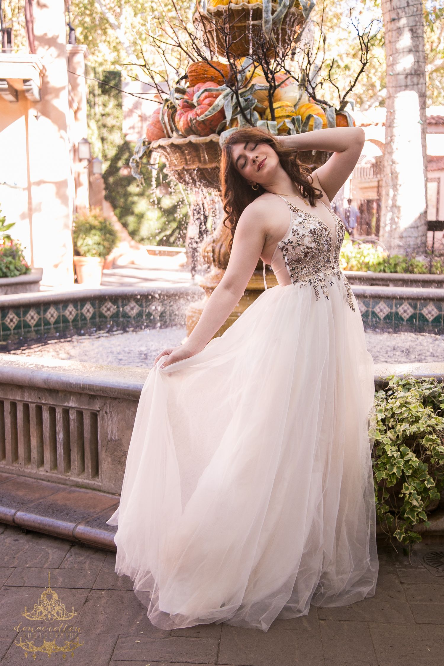 Bride in floral embroidered tulle ball gown poses gracefully beside an ornate outdoor fountain.