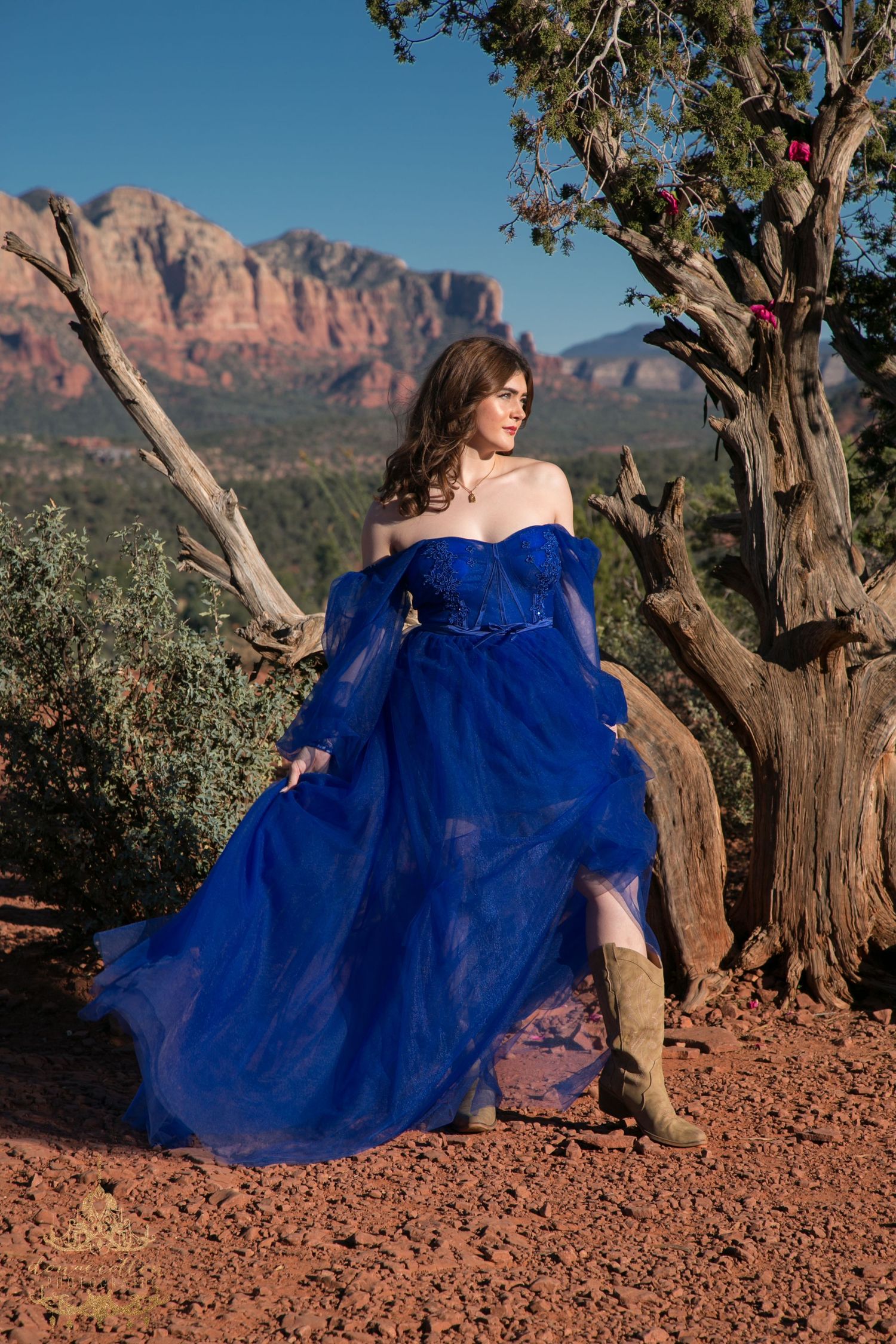 Woman in royal blue off-shoulder tulle gown with boots poses near desert tree in Sedona.