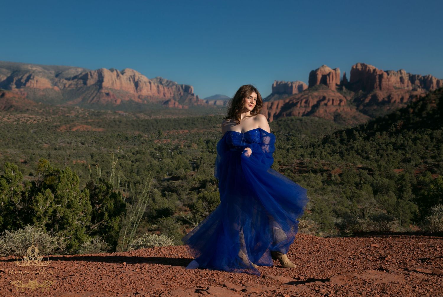 Woman in royal blue tulle gown stands before stunning Sedona red rock landscape panorama.