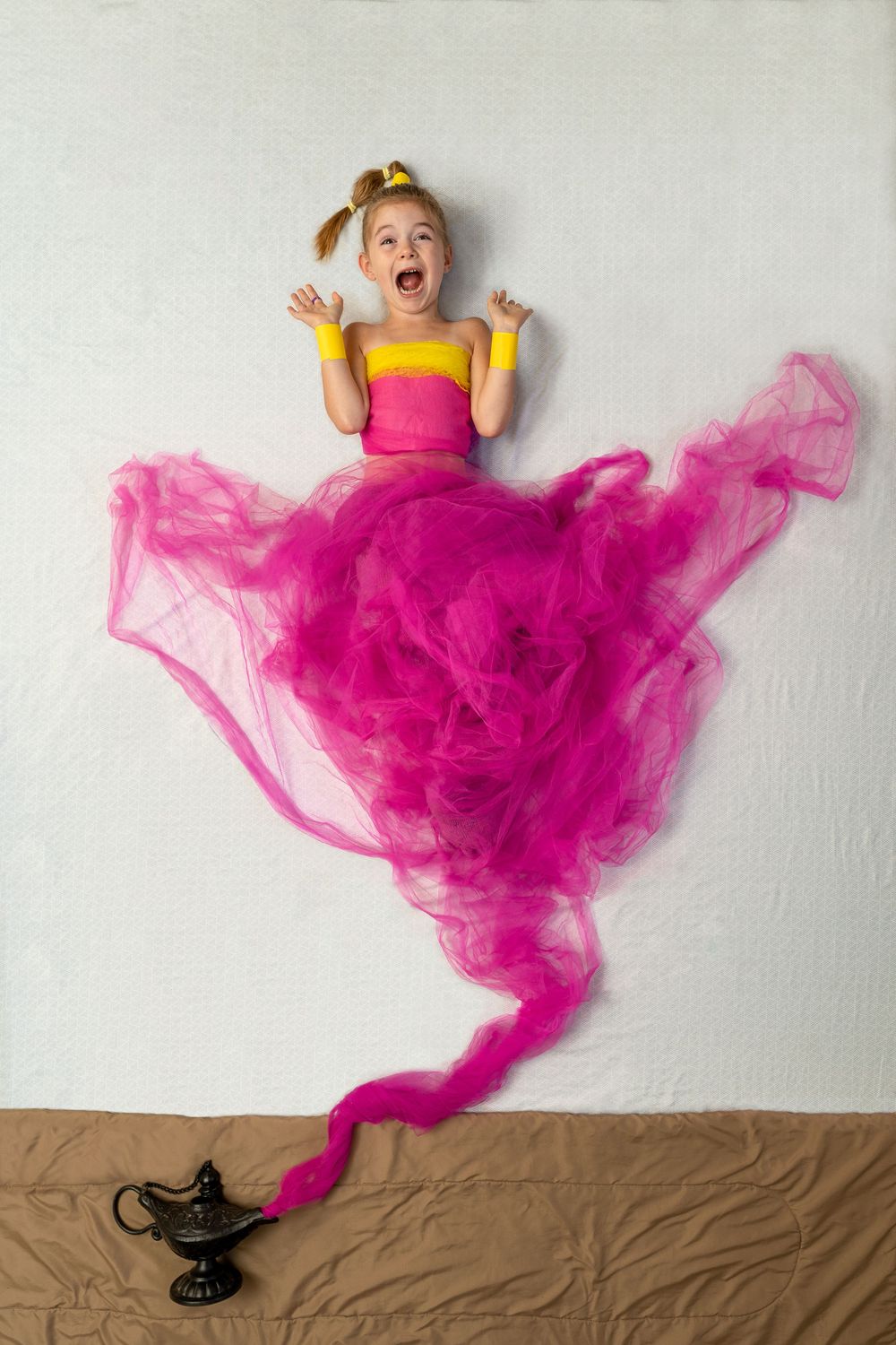 Creative photo of a yellow and pink dress with flowing tulle fabric appearing to emerge from a magic lamp.