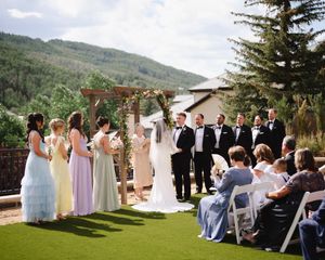 Panoramic view of an outdoor wedding ceremony in a mountainside setting with guests seated on white chairs.
