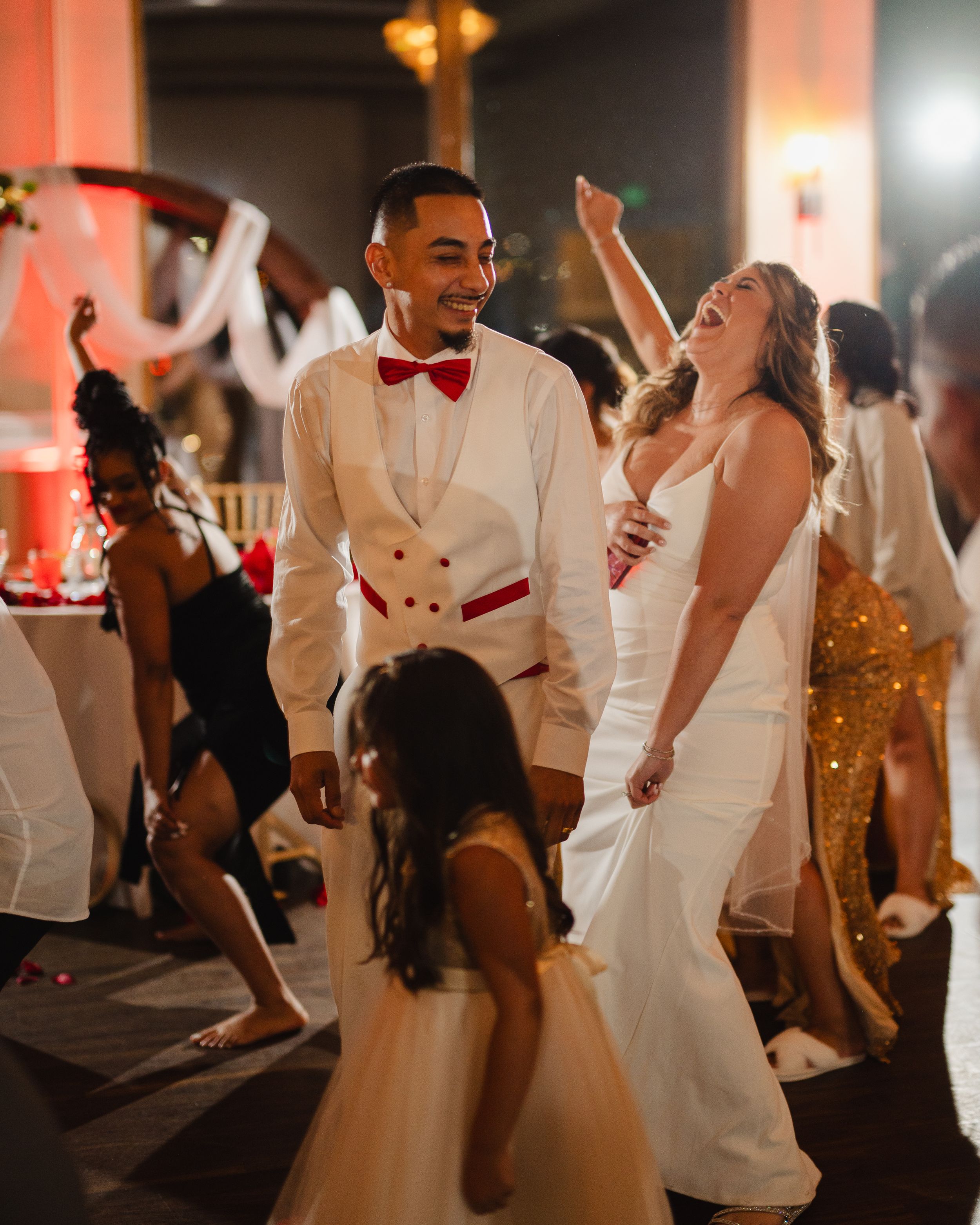Wedding reception dance floor filled with guests in white attire celebrating.