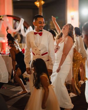 Wedding reception dance floor filled with guests in white attire celebrating.