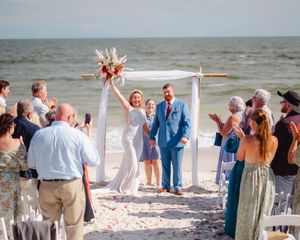 Happy celebration at a beach wedding ceremony as guests cheer for the newlyweds under a white arch on a sunny day.