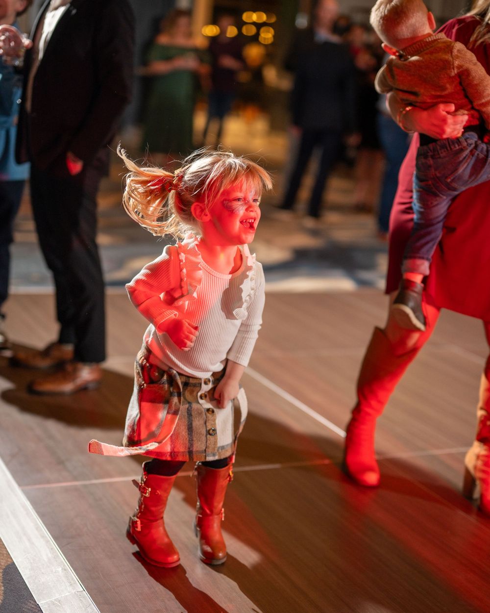 People dancing on a wooden floor illuminated by red stage lighting.