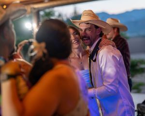 Wedding reception dance party with guests in cowboy hats under blue evening lighting.