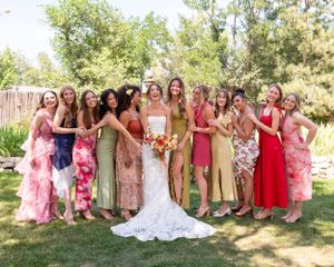 A group in colorful dresses poses together on a sunny day in a garden setting.