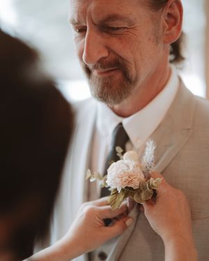 Close-up of boutonniere being pinned on light colored suit jacket.