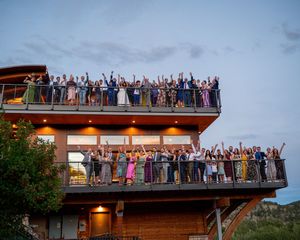 Large group celebrating on multi-level wooden deck with mountain backdrop.