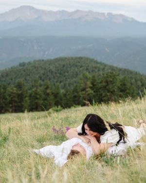 Couple laying in mountain meadow with scenic mountain vista backdrop.