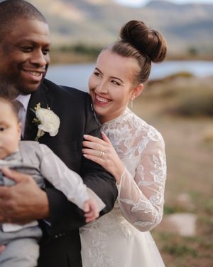A romantic wedding couple embraces outdoors in a scenic mountain landscape wearing traditional formal attire.