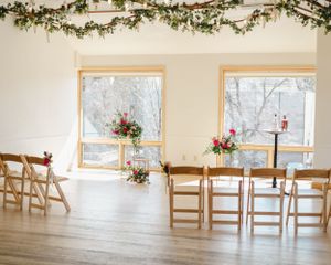 Elegant wedding venue with wooden chairs and floral garland decorations by sunlit windows.