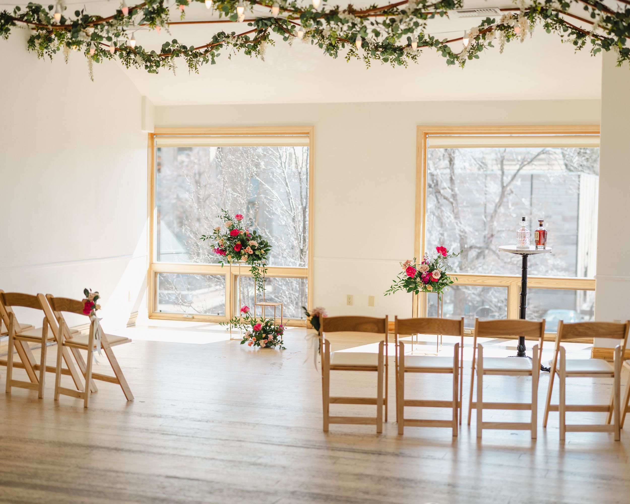Elegant wedding venue with wooden chairs and floral garland decorations by sunlit windows.