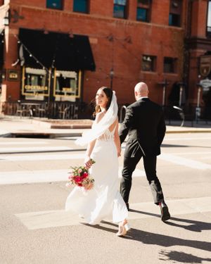 Newlyweds crossing a city street with bride holding a vibrant pink bouquet.