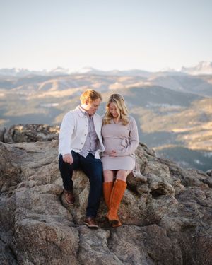 Couple sitting together on mountain peak overlooking scenic winter landscape.