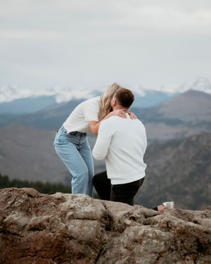 Couple sharing intimate moment on rocky mountain overlook during sunset.