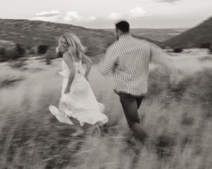 A couple runs through a desert landscape with the bride's white dress flowing in the wind.