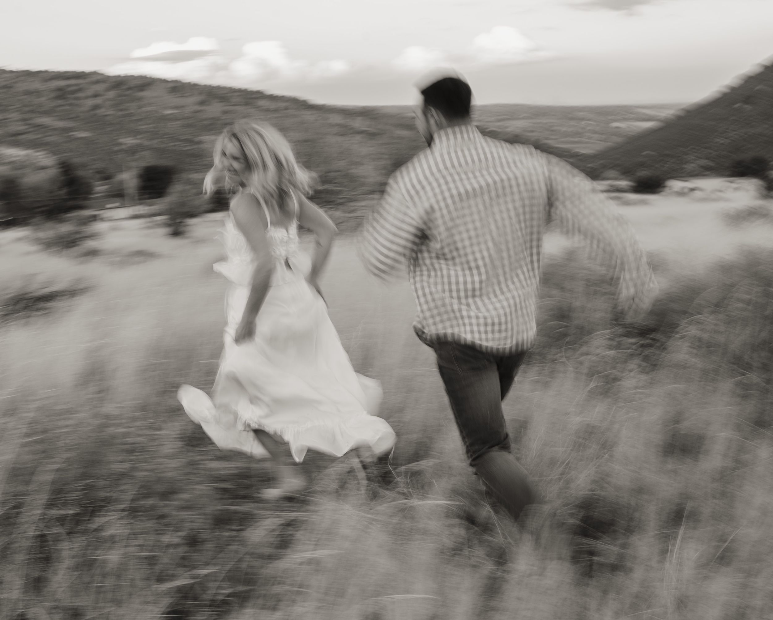 A couple runs through a desert landscape with the bride's white dress flowing in the wind.