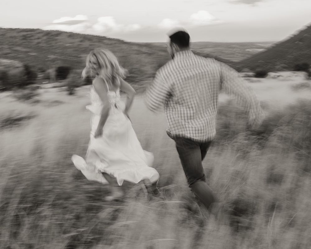 A couple runs through a desert landscape with the bride's white dress flowing in the wind.