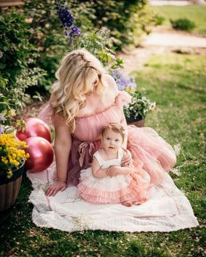 Mother and daughter in matching pink dresses having a garden photoshoot with flowers and balloons.