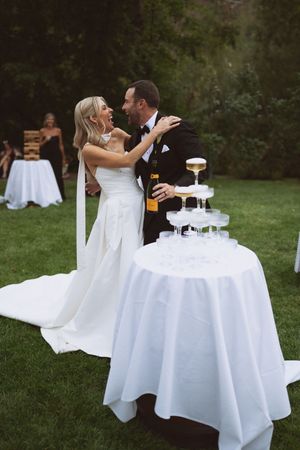 Bride and groom laughing together beside a champagne tower at an elegant outdoor wedding reception.