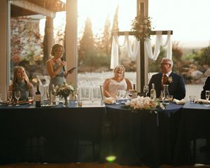 Wedding reception toast with guests seated at a decorated head table, bathed in warm golden sunset light.