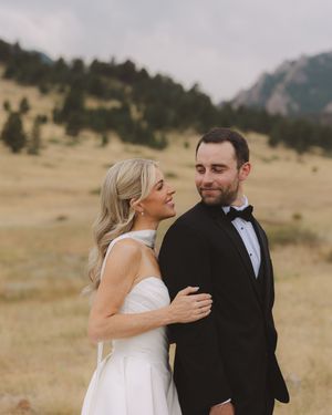Bride and groom pose in golden meadow with Rocky Mountain backdrop on their wedding day.