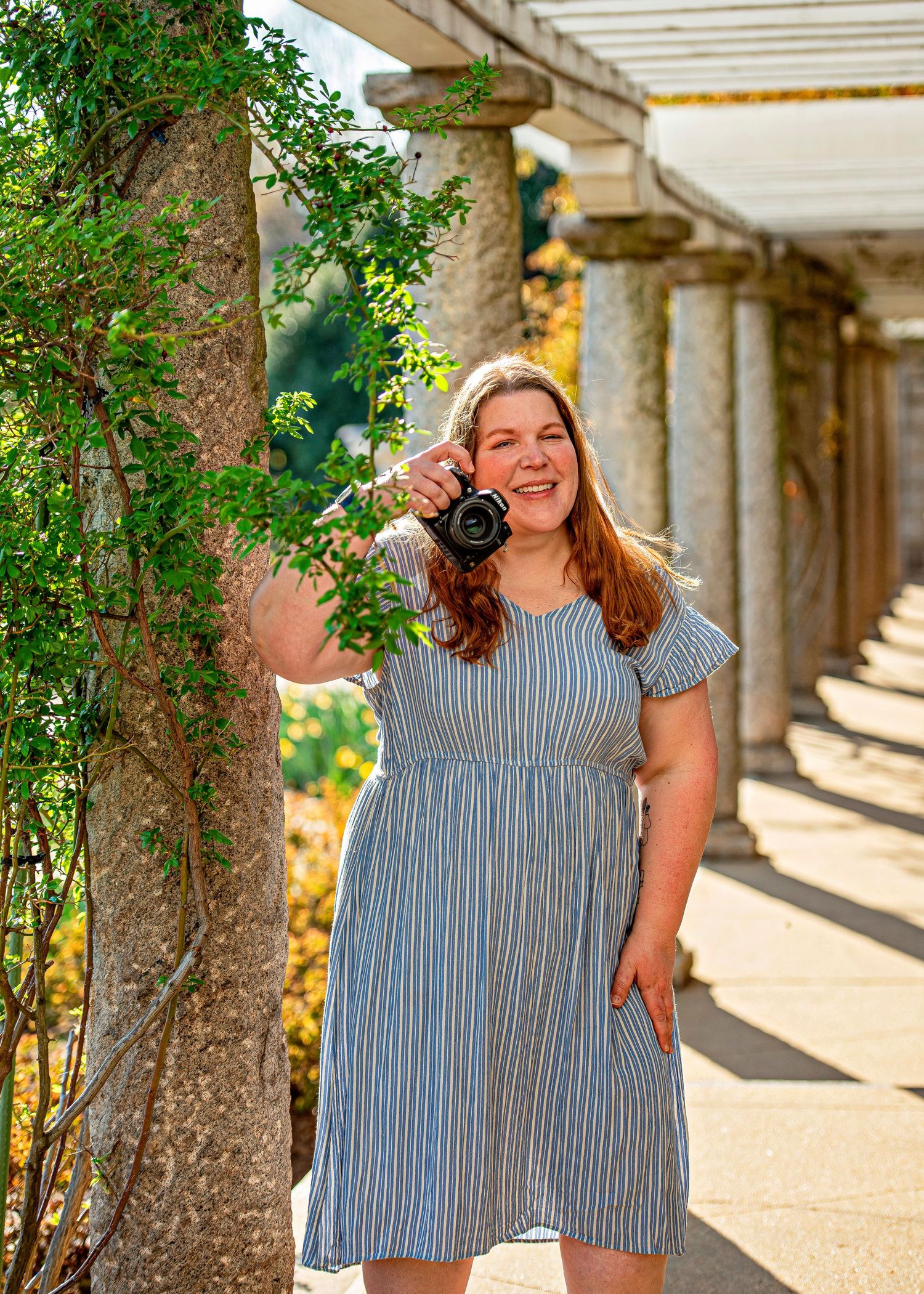 A photographer in casual attire holds camera gear against a white background.