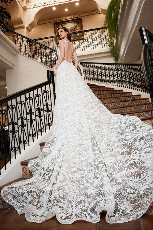 A stunning lace wedding dress with a dramatic cathedral train cascades down an elegant staircase with wrought iron railings.