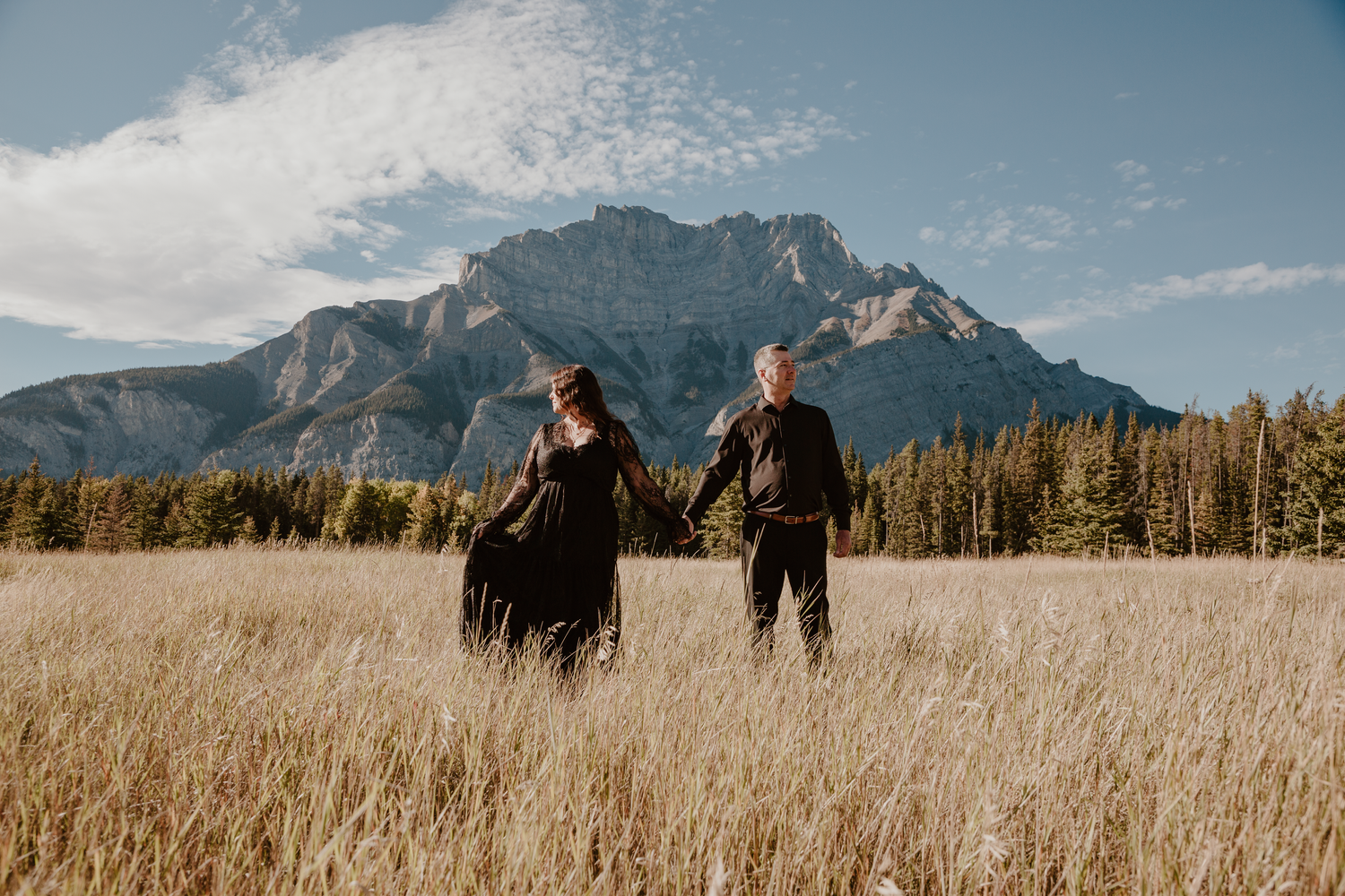 Couple wearing black holding hands looking different ways with a mountain backdrop