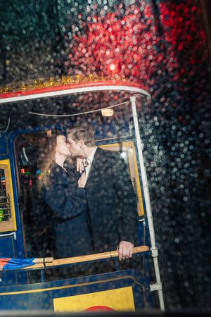 Couple sharing a romantic kiss inside a cable car on a rainy night.