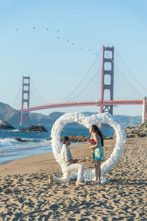 Marriage proposal on Baker Beach with heart floral arch and Golden Gate Bridge.