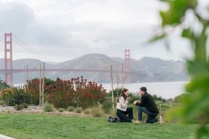 Man proposing to woman on one knee with Golden Gate Bridge backdrop.