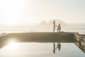 Silhouette of marriage proposal reflected in water at sunset by the ocean.