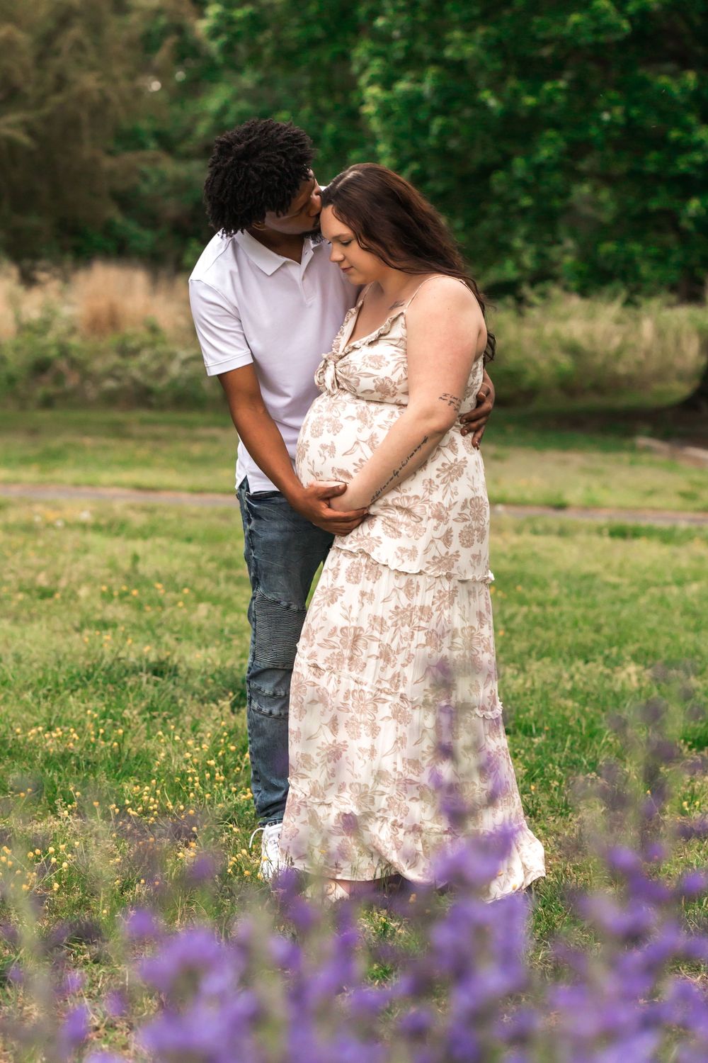 A couple shares an intimate moment in a field of purple wildflowers during golden hour.