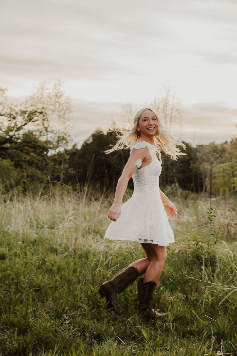 Senior girl spins in a short, white dress in a field of Prairie grass at Retzer Nature Center in Waukesha, Wisconsin.