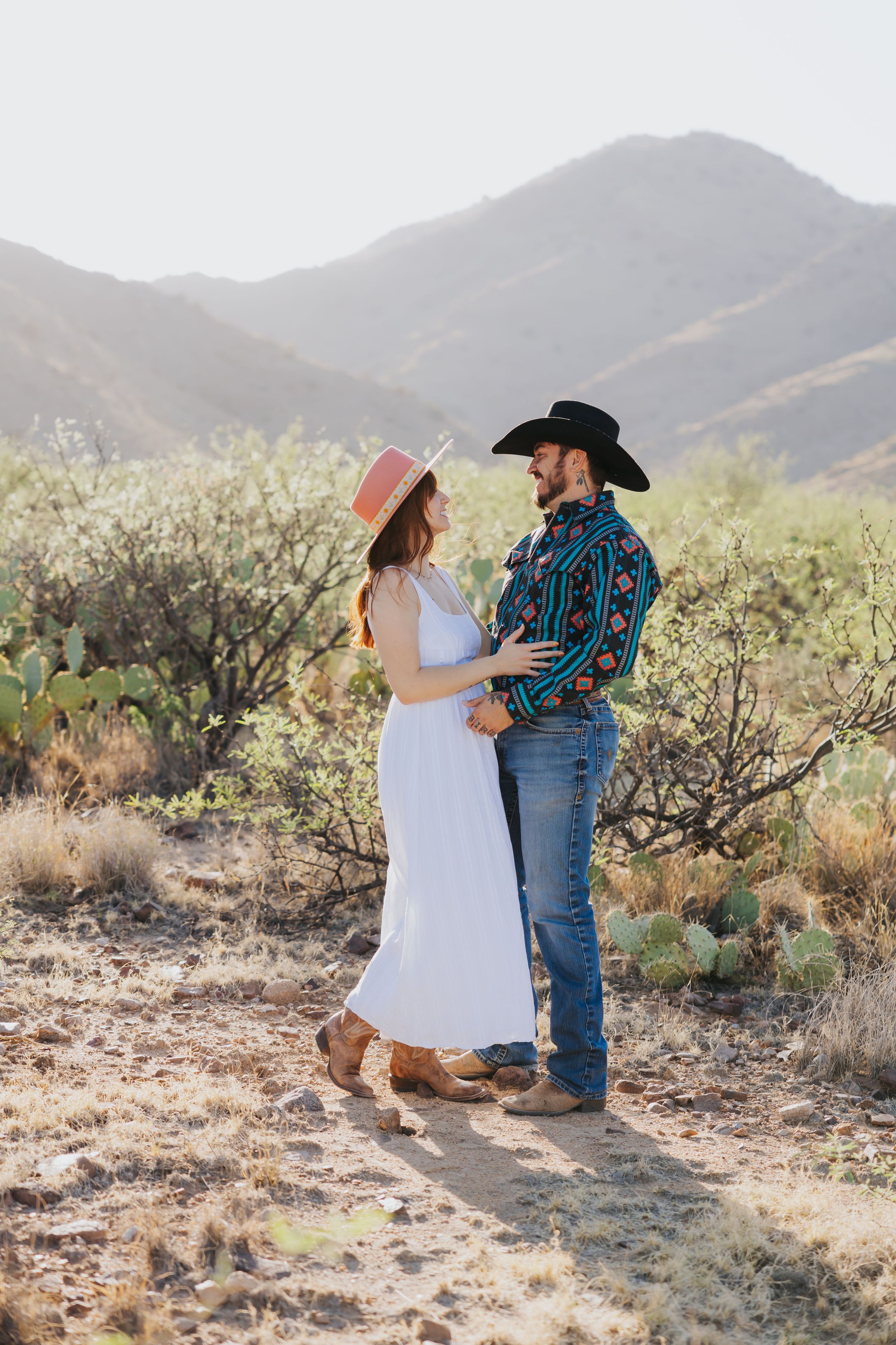 A romantic couple dances together in a desert setting with mountains and cacti.