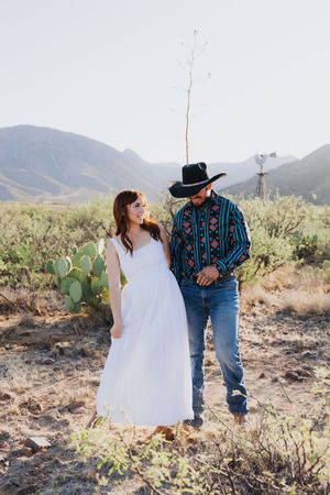 A couple enjoys a candid moment in a desert setting with mountains.